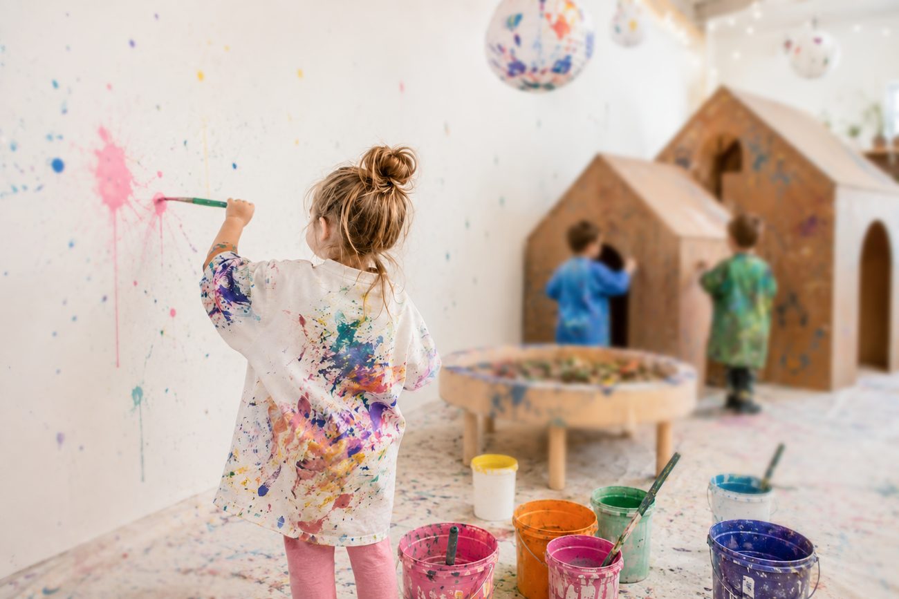 A child painting freely at a wall covered in colour
